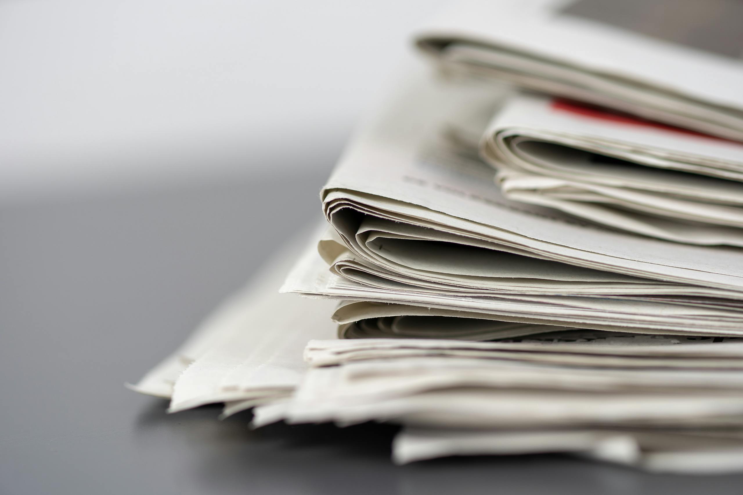 Close-up of stacked newspapers on a table, representing media and journalism.